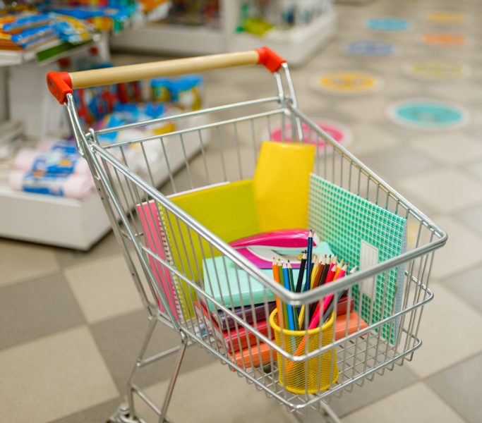 Cart with office supplies between the shelves in stationery store, nobody. Assortment in shop, rows of accessories for drawing and writing, school equipment